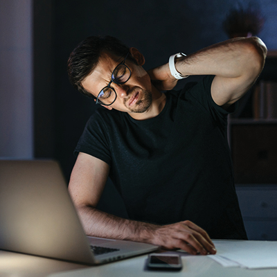 Man rubbing neck in discomfort while working from des at home